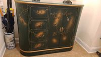 Full view of green bow front cabinet showing painted bird and flower motifs with brass pulls and glass top.