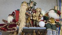 Wide view of assorted Christmas figurines displayed on a shelf with light gray concrete wall background.