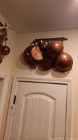 Copper cookware set of seven items hung on wooden rack above doorway including pans, bowls, and hanger