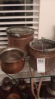 Three copper pots on glass shelf with visible patina and oxidation, one with curled legs