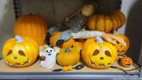 Full shelf view showing seven pumpkins, two ghost food spreaders, and a scarecrow lying on pumpkins.