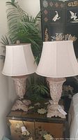 Two decorative resin table lamps with beige linen shades on a decorative chest in a bedroom setting