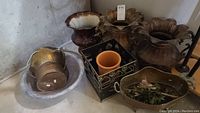 Lot of 9 assorted planters including ceramic, metal, copper, terracotta in basement setting showing some dirt and wear