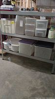 Shelving unit with nine plastic storage containers of different sizes and colors, cloth storage basket, and decorative tins.