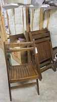 Set of six vintage wooden folding chairs in basement, some stacked and one open chair visible, showing wooden slatted construction and natural patina.
