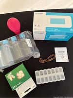 View of assorted items: box of face masks, silicone earplugs, pill organizer, travel containers, and a copper bracelet arranged on a black surface.