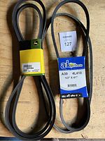Photo showing two replacement belts, one John Deere labeled black belt and one A&I Products labeled belt.