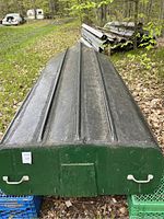 Boat upside down showing black hull bottom with ridges and green stern end with handles