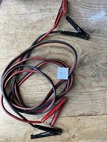 Booster cables coiled on wood showing red and black clamps with wire insulation, identified as lot 65.