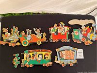 Full set of six Disney themed wooden train car wall hangings laid out on black surface showing characters and condition.