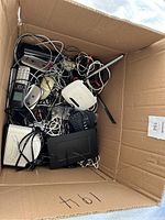 Overview of the box filled with assorted electronic items including remotes, router, and projector among tangled cords