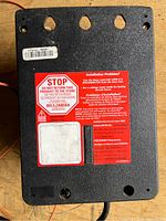 Back side of the electric fence energizer showing warning label and mounting holes.