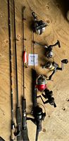 Five fishing rods and five fishing reels arranged on wooden surface