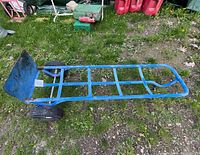 Blue metal hand truck with two wheels and flat base plate on grass surface, showing wear and some rust.