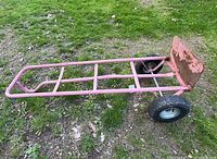 Side angle view of red hand truck furniture dolly showing tubular metal frame, flat base plate and pneumatic wheels on grass.
