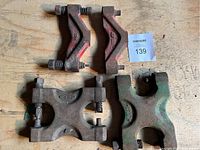 Top view of four metal farm equipment parts on plywood surface, showing two red angled brackets and two green clamp parts.