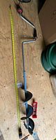 Side view of the full five foot hand ice auger showing the ergonomic handle and crank, next to a tape measure confirming length.