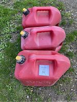 Top view of three red plastic Jerry cans placed on grass showing handles and black caps with yellow pour spouts
