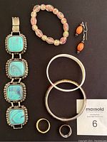 Photo of the assorted jewelry laid out including turquoise multi-link bracelet, bead bracelet, two bangles, two rings, and drop earrings with orange beads.