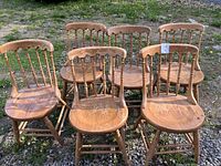 Front view of six wooden kitchen chairs with rounded backs arranged in two rows outdoors on grass.