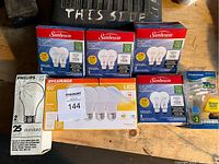 Photo showing various boxes of light bulbs from brands Sunbeam, Sylvania, Philips, and Luminuous on a table.