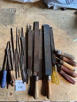 Various rasps and files spread on a wooden surface showing different sized tools with wooden and plastic handles.
