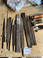 Various metal rasps and files arrayed on a wooden surface, showing different profiles and large to small sizes. Several have rust or wear marks.