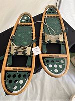 Pair of adult wooden snowshoes with green decking and laced wooden frames, laid flat with visible foot bindings and adjustment laces.