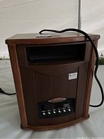 Front view of Comfort Furnace space heater showing wooden-style casing, vent grille and electronic control panel with buttons.