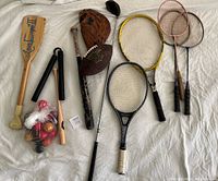 Lot of assorted sports equipment including various rackets, bat, football, glove and pool balls on white background.