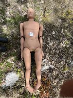 Photo of the full-body firefighter training mannequin lying on the ground outdoors showing its head, torso, and joints at shoulders, elbows, hips, knees, and ankles.