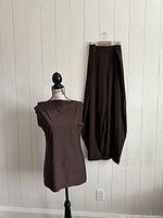 Full view of brown sleeveless top on mannequin and matching long skirt hung on hanger against white wall.