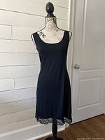 Front view of black slip dress with lace trim on mannequin against white wall