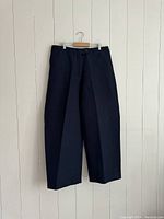 Front view of navy wide leg pants hanging on a wooden hanger against a white wall.
