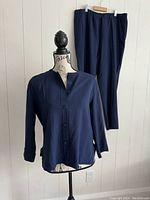 Front view of navy blue button-up jacket on mannequin with matching pants hanging on hanger in background