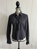 Front view of the black iBlues blouse on mannequin showing the ruffled button placket and collar