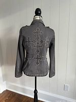 Rear view of gray women's jacket showing large cross embroidery on back and tailored seams.