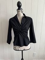 Front view of the black top showing the ruched detail and collar on a mannequin.
