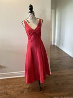 Front view of red Nicole Miller dress on mannequin showing deep V neckline, sleeveless design, fitted bust, bow detail at waist, and A-line skirt.
