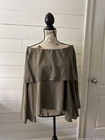 Front view of off shoulder tiered blouse on mannequin, showing layered design and cactus color.