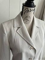 Close-up front view of the cream/light beige suit jacket collar, lapel, and buttons on a mannequin form showing stitching details.