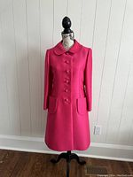 Full-length front view of pink coat on mannequin against white wall and hardwood floor