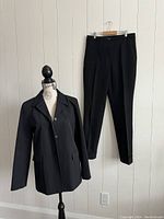 Front view of black Teen Flo jacket on mannequin and matching pants hanging on wall hook.