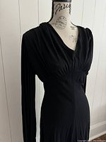 Front three-quarter view of the dress on a mannequin showing draped neckline, empire waist, and sleeve length