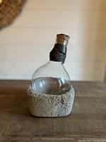 Glass wine decanter showing the full setup with concrete base, leather wrapped neck, and cork stopper on wooden table