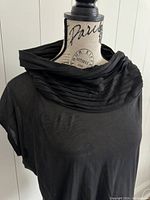 Front view of the black Yigal Azrouël top showing the pleated draped neck on a mannequin against a white paneled background.