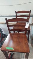 Photo showing two wooden high back bar stools with visible wear, placed against a white wall.