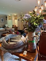 View of gray woven cloth basket and tall decorative vase with faux purple flowers on wooden table in living room setting.