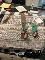 Photo showing one of the woven tote bags with diamond and stripe pattern, leather-like strap, tassel, and copper crescent moon and star ornament with hanging bells attached.