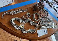 Overview of jewelry lot laid out on wooden table showing bracelets, earrings, necklace, and chains.